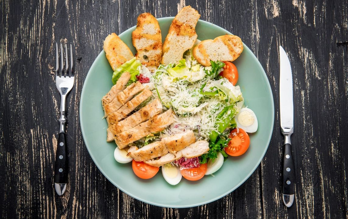 Ein Caesar-Salat mit gegrilltem Hähnchenbrustfilet, knackigem Römersalat, Kirschtomaten, gekochten Eiern, Parmesan und Croutons.
